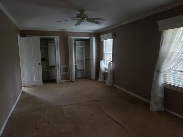 unfurnished bedroom featuring ceiling fan, two closets, ornamental molding, and multiple windows