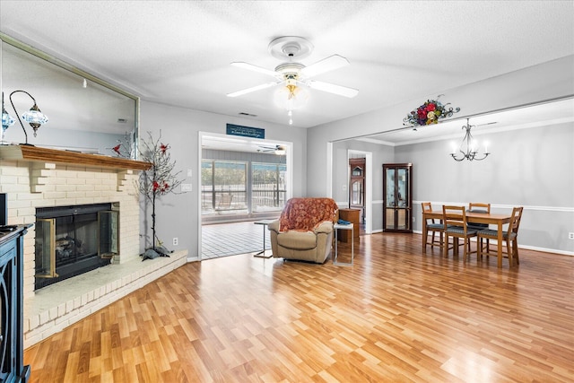 living room with a textured ceiling, hardwood / wood-style floors, ceiling fan with notable chandelier, and a brick fireplace