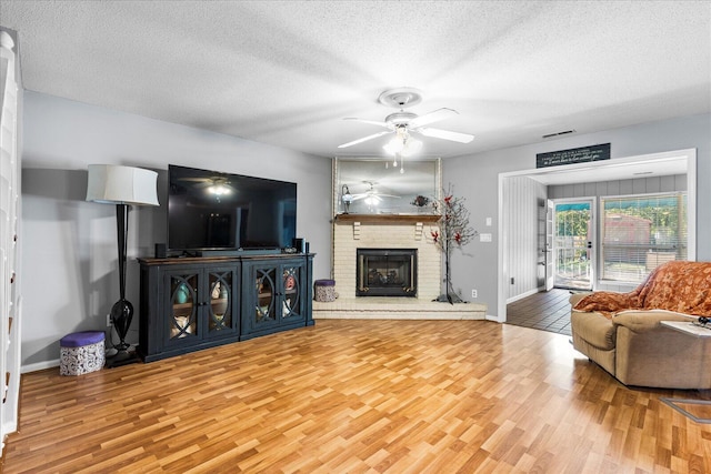 living room with ceiling fan, wood-type flooring, a textured ceiling, and a brick fireplace