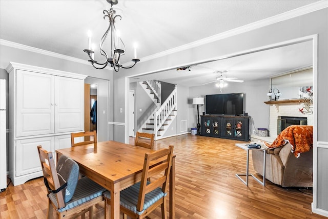 dining area with light wood-type flooring, a brick fireplace, ornamental molding, ceiling fan with notable chandelier, and a textured ceiling