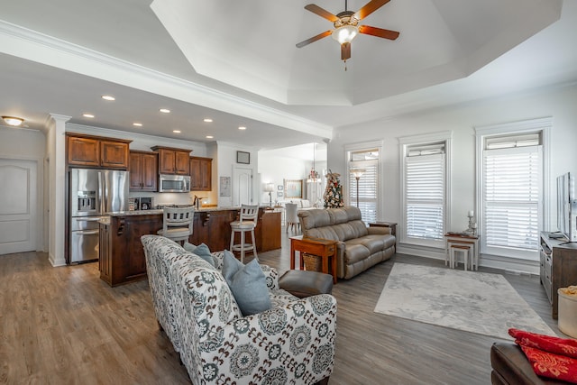 living room with dark hardwood / wood-style floors, ceiling fan, a raised ceiling, and ornamental molding