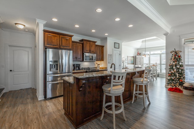 kitchen with a large island, stainless steel appliances, dark hardwood / wood-style floors, crown molding, and a breakfast bar area