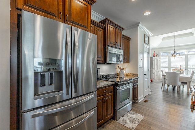 kitchen featuring stainless steel appliances, an inviting chandelier, dark stone countertops, hardwood / wood-style floors, and ornamental molding