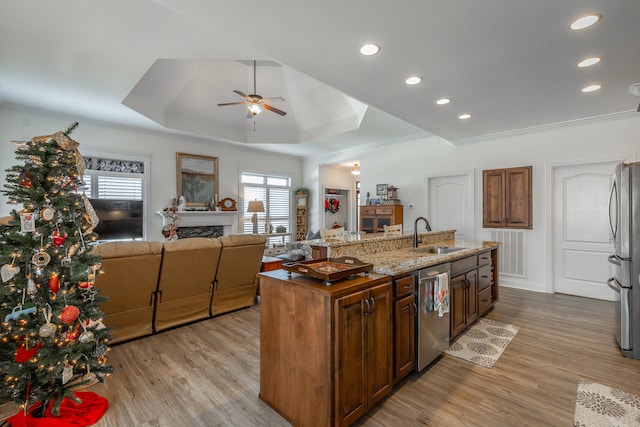 kitchen featuring light hardwood / wood-style floors, a raised ceiling, an island with sink, and appliances with stainless steel finishes