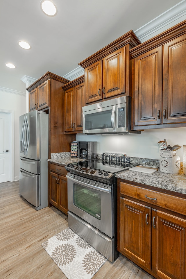 kitchen with crown molding, light wood-type flooring, light stone counters, and appliances with stainless steel finishes