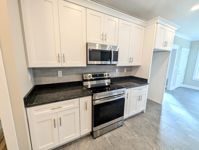 kitchen with appliances with stainless steel finishes, dark stone countertops, white cabinets, backsplash, and ornamental molding