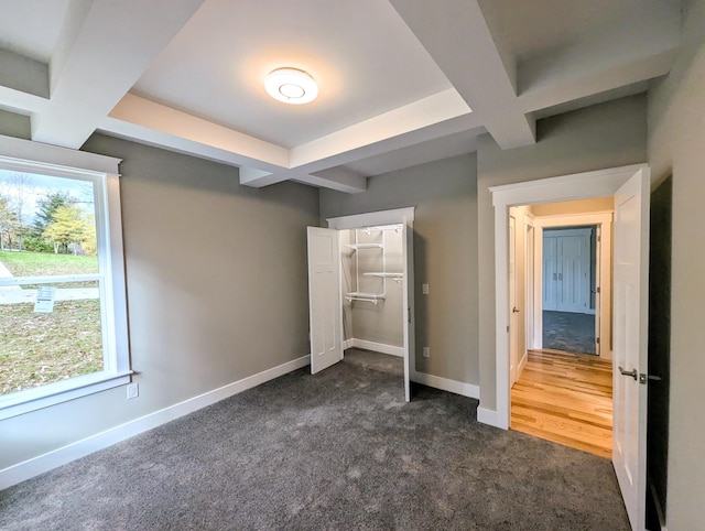 unfurnished bedroom featuring coffered ceiling, beam ceiling, multiple windows, and dark colored carpet