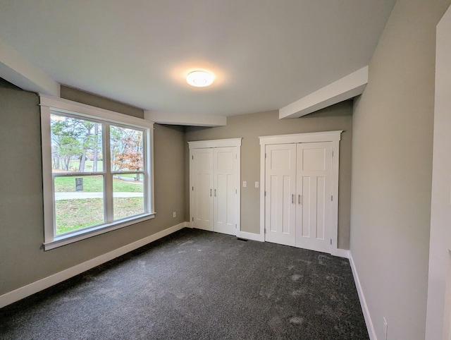 unfurnished bedroom with multiple closets and dark colored carpet