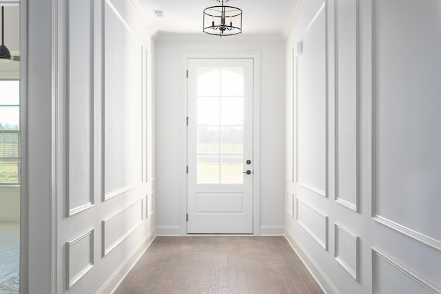 doorway featuring light hardwood / wood-style floors, an inviting chandelier, plenty of natural light, and ornamental molding