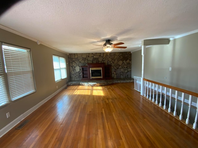 unfurnished living room with ornamental molding, a textured ceiling, ceiling fan, wood-type flooring, and a fireplace