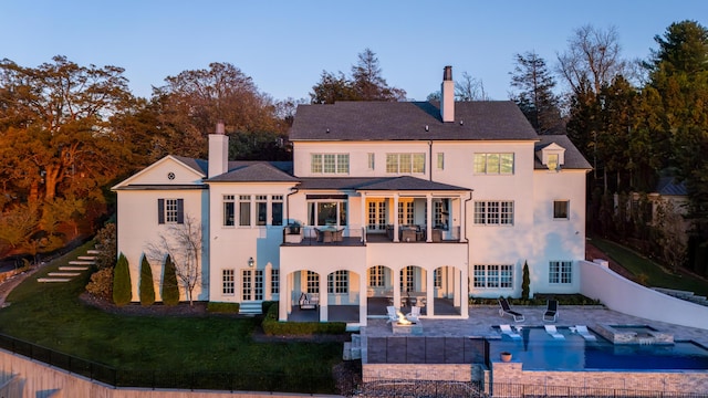 back of property featuring a swimming pool with hot tub, a balcony, and a patio area