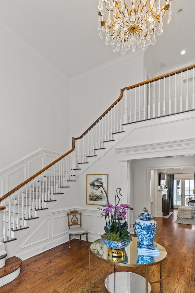 interior space featuring wood-type flooring, ornamental molding, a towering ceiling, and a chandelier