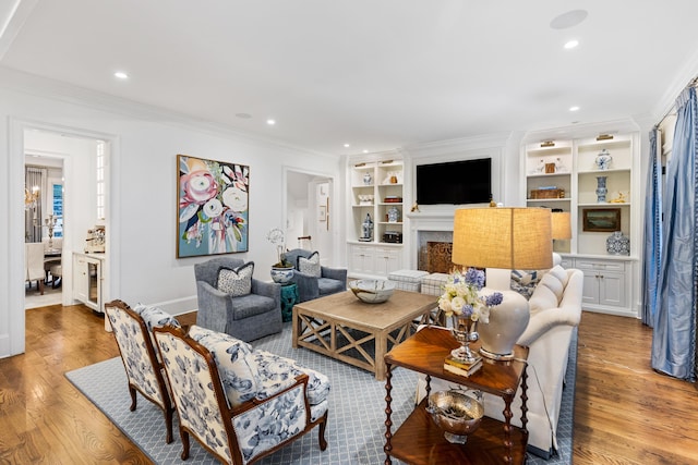 living room with built in features, light hardwood / wood-style floors, and ornamental molding