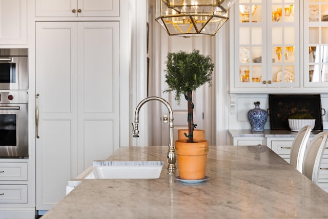 kitchen with light stone countertops, white cabinetry, hanging light fixtures, and sink