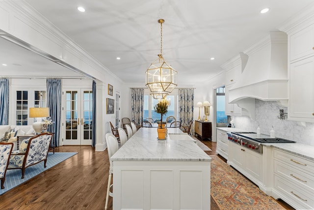 kitchen featuring custom range hood, stainless steel gas cooktop, dark wood-type flooring, a kitchen island, and hanging light fixtures