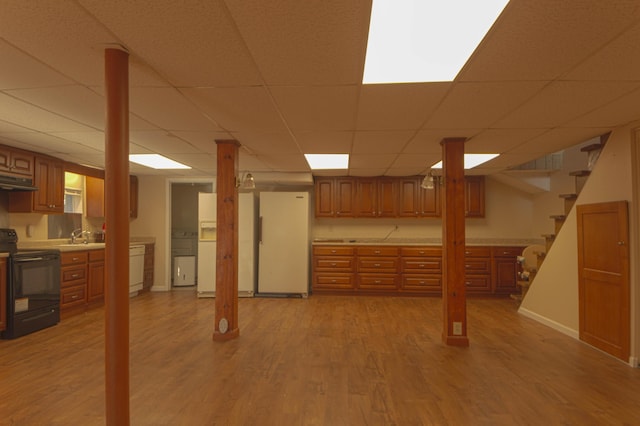 basement featuring light wood-type flooring, a paneled ceiling, sink, white refrigerator, and white fridge with ice dispenser