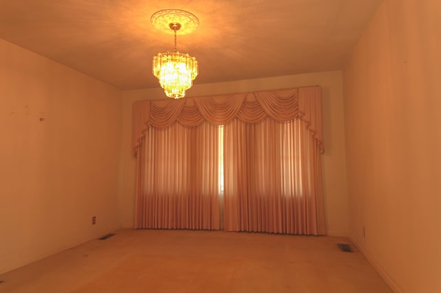 unfurnished room featuring carpet and an inviting chandelier