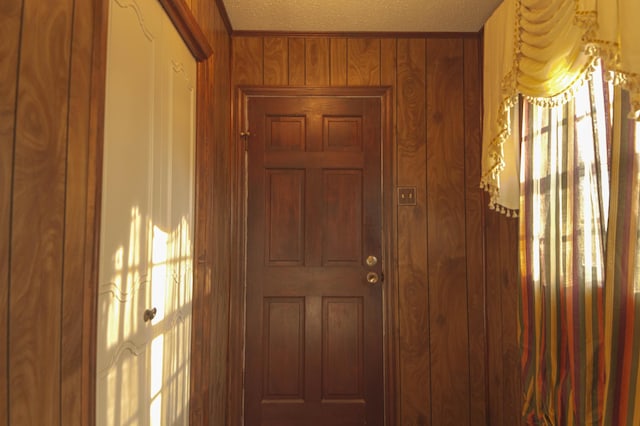 doorway to outside featuring a textured ceiling and wooden walls