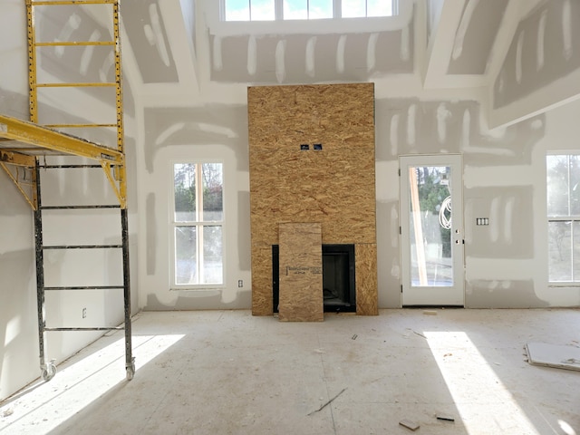 unfurnished living room featuring a healthy amount of sunlight, a stone fireplace, and a high ceiling