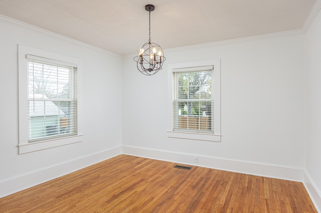 empty room featuring hardwood / wood-style flooring, an inviting chandelier, and crown molding