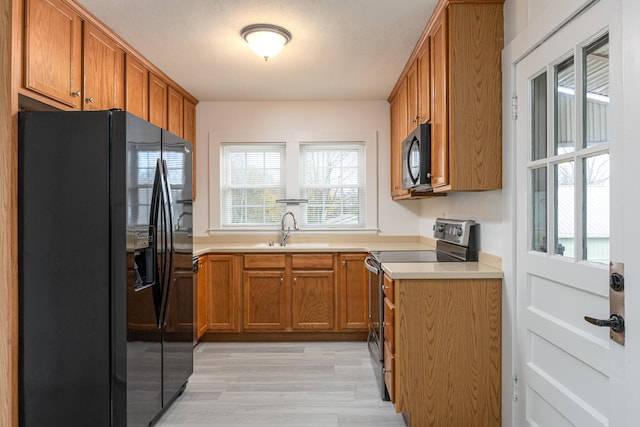 kitchen featuring black appliances, a textured ceiling, sink, and light hardwood / wood-style flooring