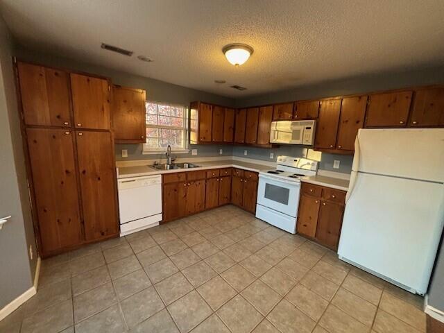 kitchen with a textured ceiling, white appliances, light tile patterned floors, and sink