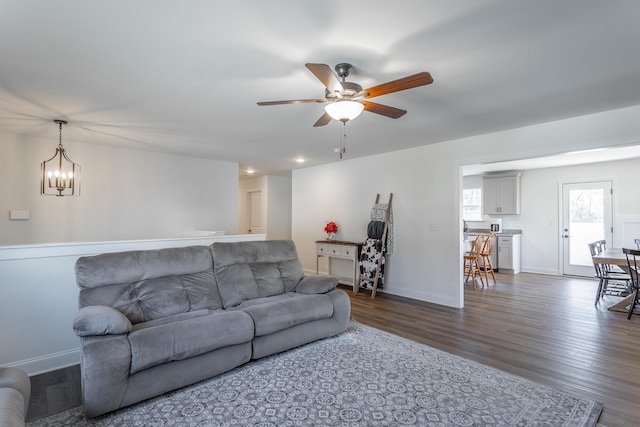 living room with ceiling fan with notable chandelier and dark hardwood / wood-style flooring