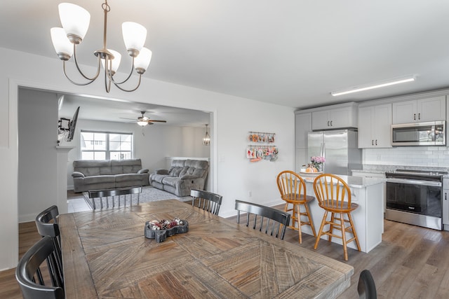 dining space with ceiling fan with notable chandelier and dark wood-type flooring