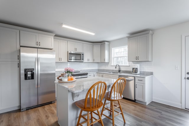 kitchen featuring sink, a center island, stainless steel appliances, light stone counters, and light hardwood / wood-style floors