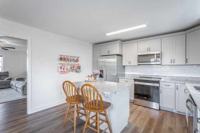 kitchen with light stone countertops, appliances with stainless steel finishes, a breakfast bar, a kitchen island, and hardwood / wood-style flooring