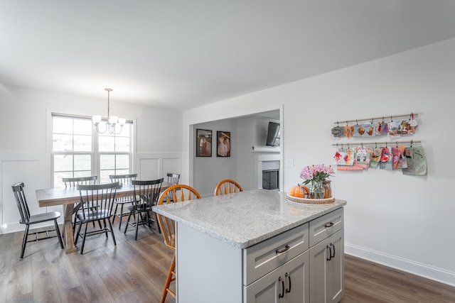 kitchen with light stone countertops, hanging light fixtures, an inviting chandelier, dark hardwood / wood-style flooring, and a kitchen island