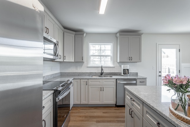 kitchen with gray cabinetry, sink, stainless steel appliances, light hardwood / wood-style flooring, and decorative backsplash