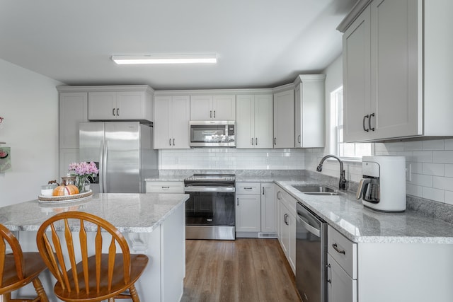 kitchen with a kitchen breakfast bar, sink, light stone counters, appliances with stainless steel finishes, and dark hardwood / wood-style flooring