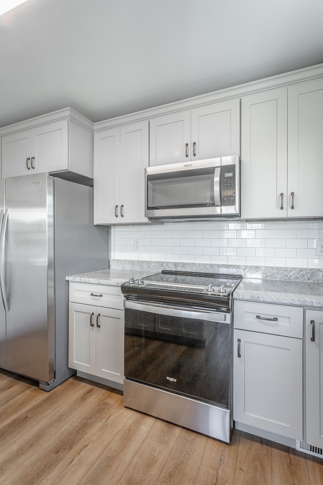 kitchen with tasteful backsplash, light hardwood / wood-style flooring, white cabinets, and stainless steel appliances