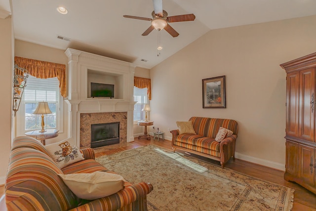 living room with a high end fireplace, light hardwood / wood-style flooring, ceiling fan, and lofted ceiling