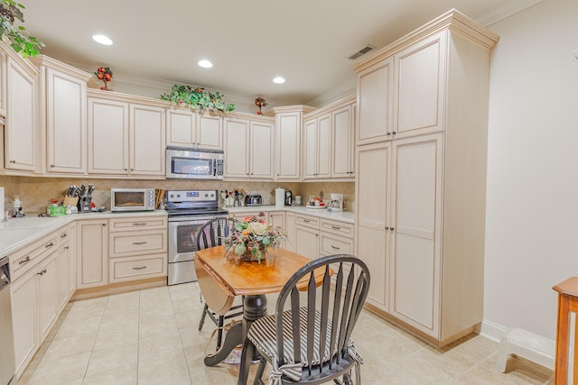 kitchen with ornamental molding, appliances with stainless steel finishes, tasteful backsplash, cream cabinetry, and light tile patterned flooring