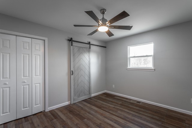 unfurnished bedroom with ceiling fan, a barn door, dark hardwood / wood-style flooring, and a closet