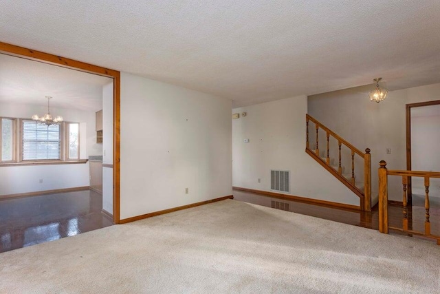 carpeted spare room with a textured ceiling and an inviting chandelier