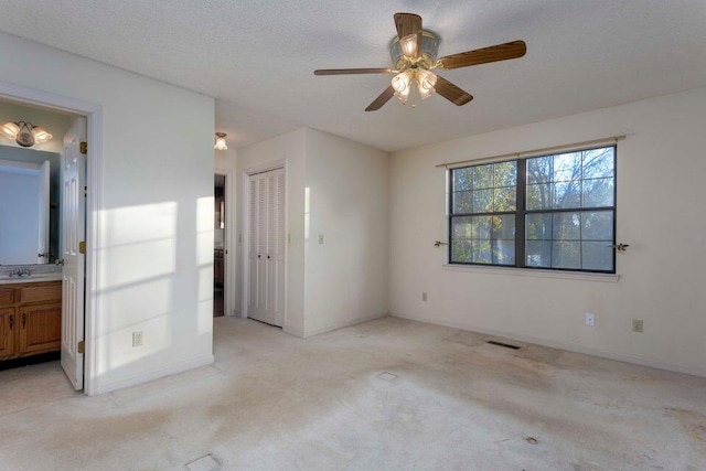 unfurnished bedroom with ceiling fan, light colored carpet, a textured ceiling, and ensuite bath