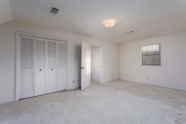 unfurnished bedroom with a textured ceiling, a closet, light carpet, and vaulted ceiling