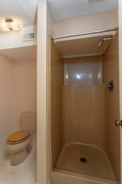 bathroom featuring tile patterned floors, toilet, a textured ceiling, and walk in shower