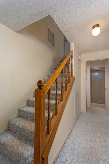 stairway with carpet and a textured ceiling