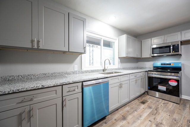 kitchen featuring sink, appliances with stainless steel finishes, gray cabinetry, light stone counters, and light hardwood / wood-style floors