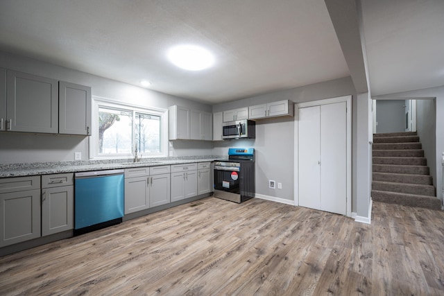 kitchen featuring sink, gray cabinets, appliances with stainless steel finishes, light stone countertops, and light wood-type flooring