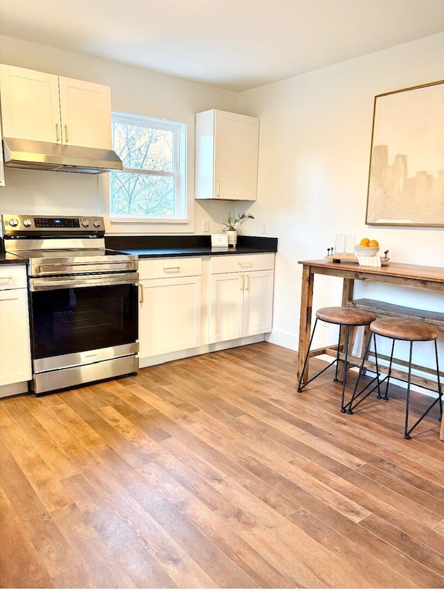 kitchen featuring electric stove, a breakfast bar, white cabinets, and light hardwood / wood-style floors