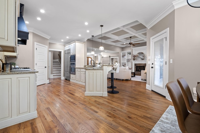 kitchen with light stone countertops, light hardwood / wood-style flooring, decorative light fixtures, and coffered ceiling