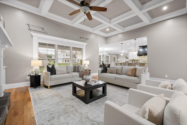 living room featuring beam ceiling, coffered ceiling, crown molding, light hardwood / wood-style floors, and ceiling fan with notable chandelier