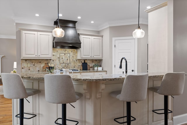 kitchen featuring custom exhaust hood, backsplash, hanging light fixtures, light hardwood / wood-style flooring, and light stone countertops