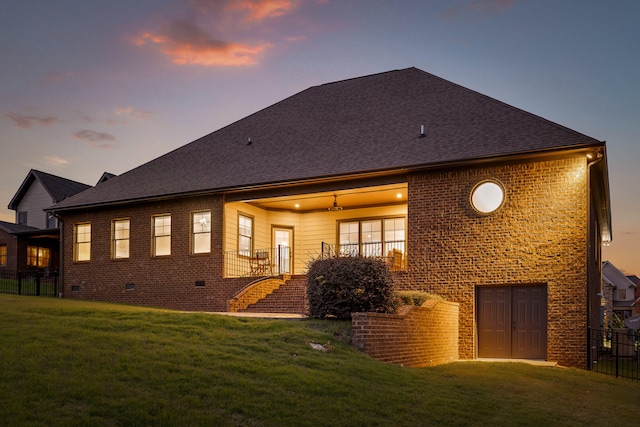 back house at dusk featuring ceiling fan and a yard