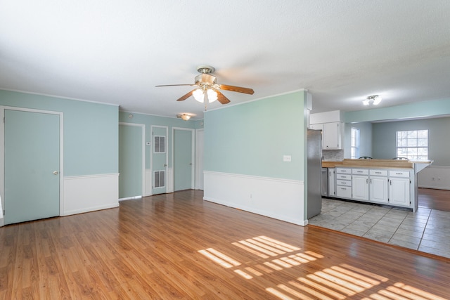 unfurnished living room featuring light wood-type flooring, ceiling fan, and ornamental molding